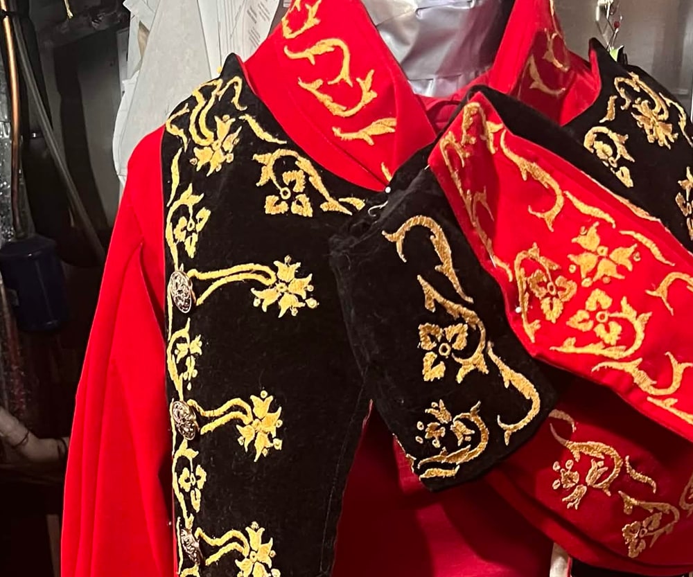 Gold floral scrollwork embroidered on the black velvet lapels and red cape of a coat, seen close up.