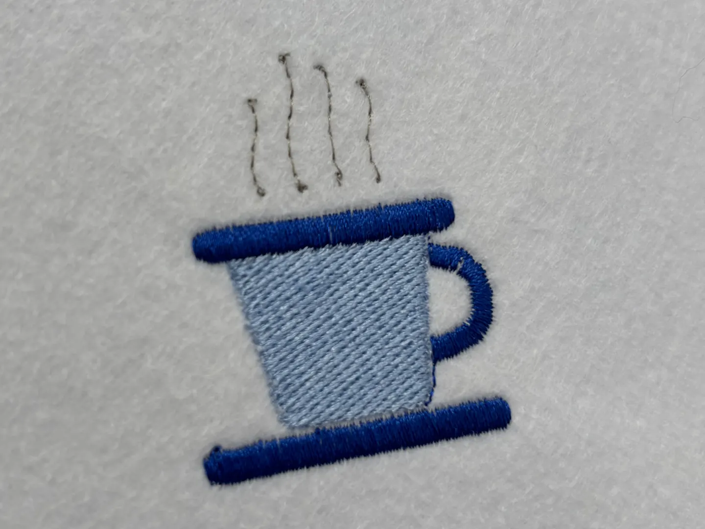 The coffee cup from Parts 4 to 6, its body filled with angled rows, its rim and handle worked as dark blue satin bands.